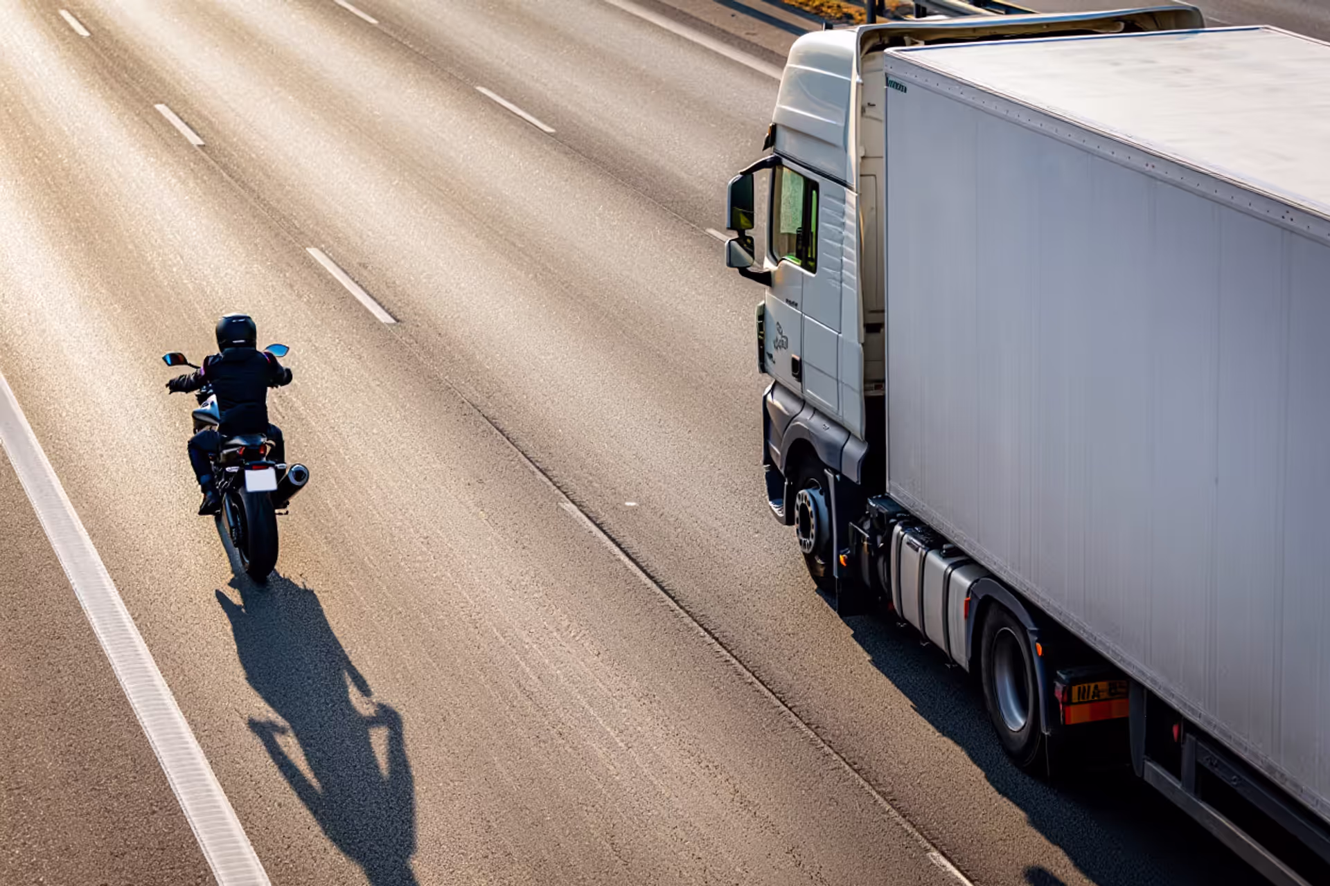 Large semi-truck and motorcyclist riding side by side on a multi-lane highway showing dramatic size difference between vehicles
