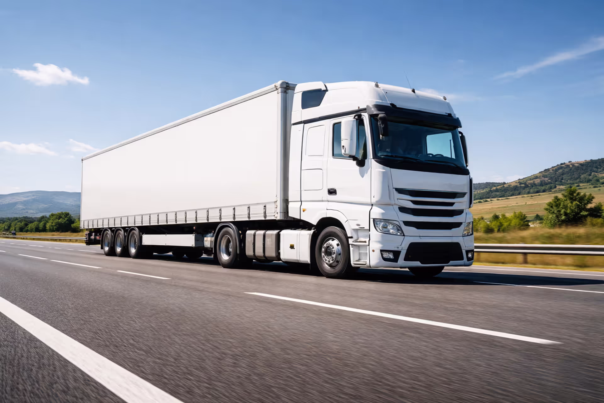 White semi-truck with trailer driving on a multi-lane highway in clear weather with road markings visible